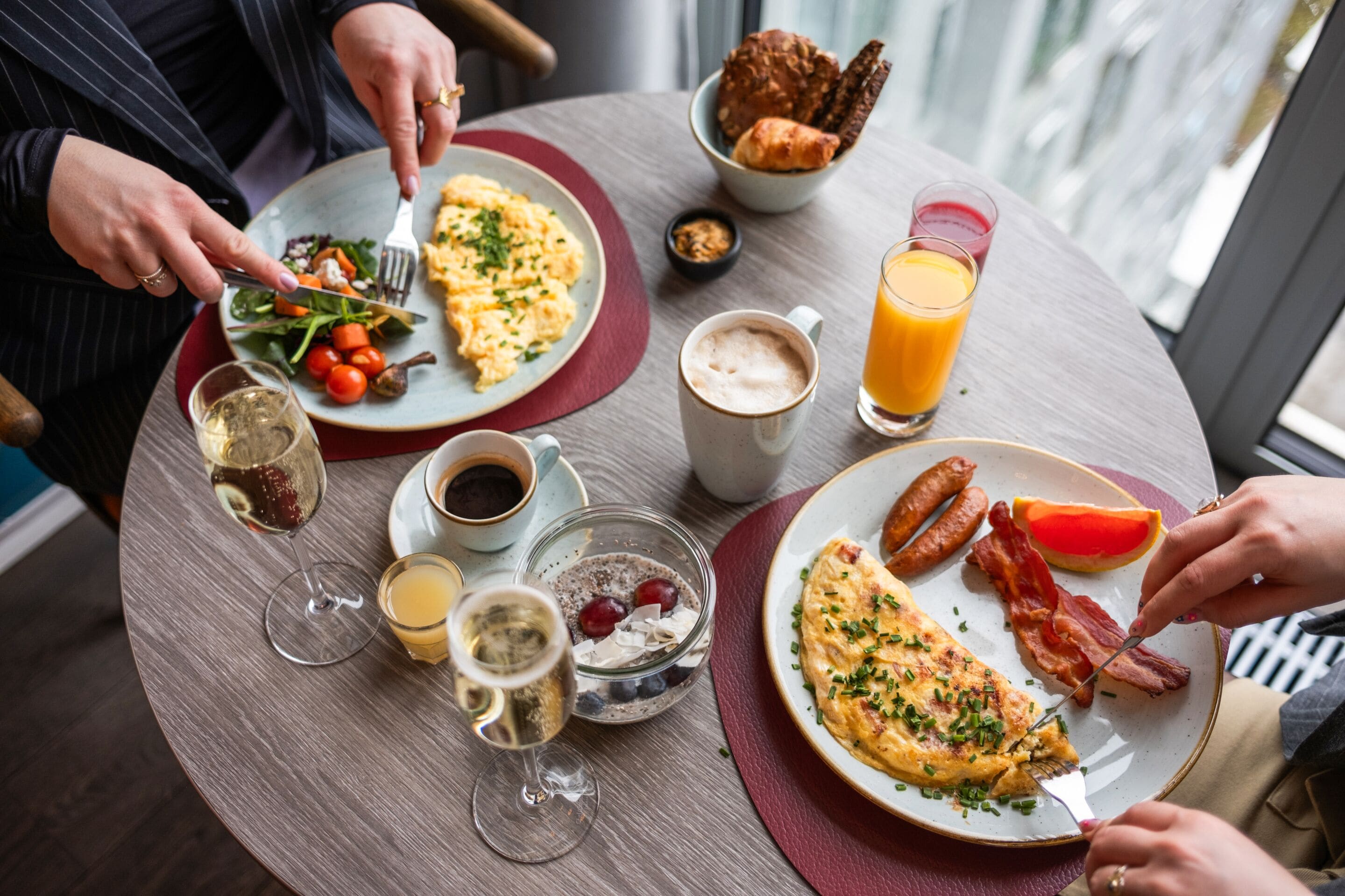 A breakfast setting with plates of food, drinks, and a window view.