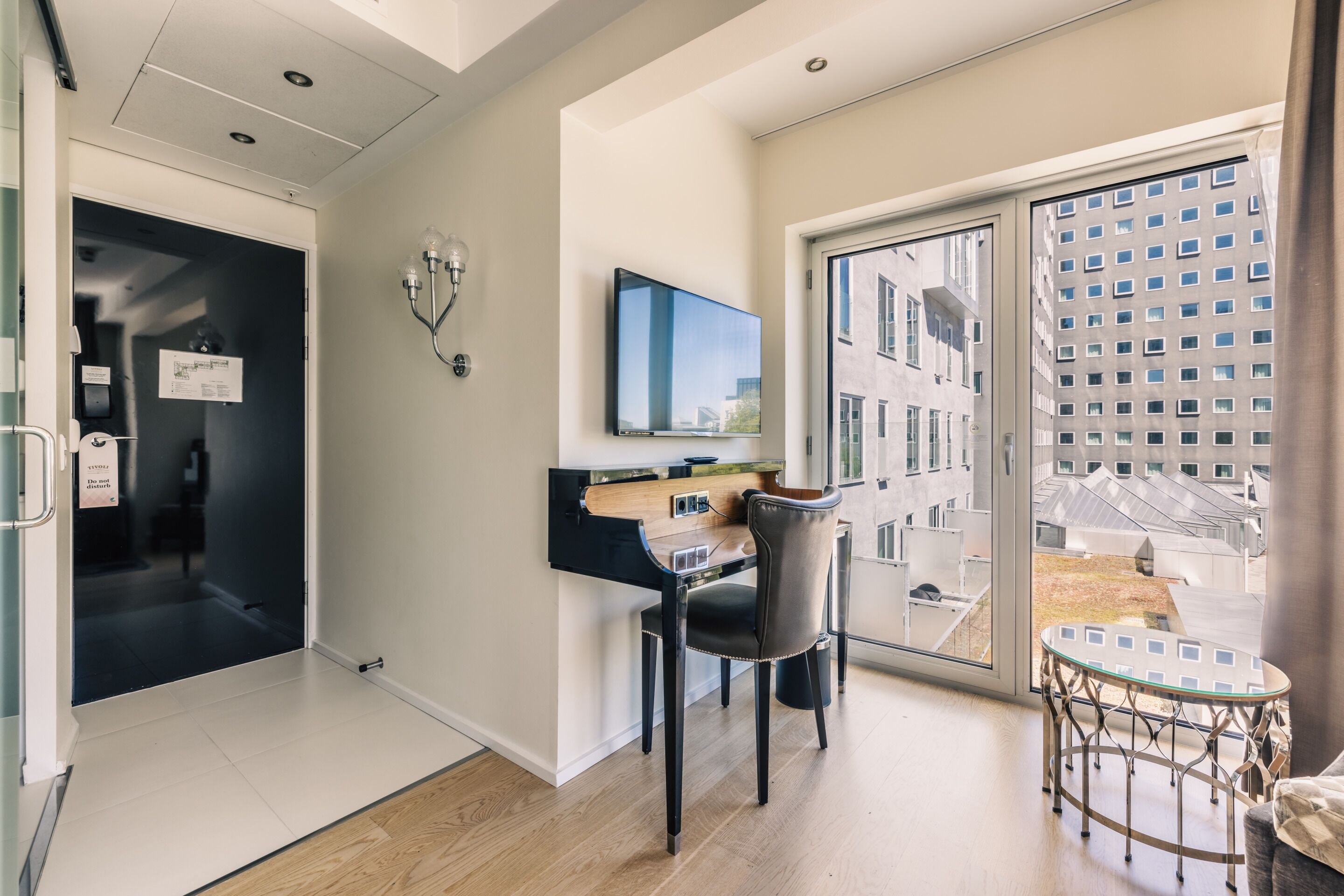 Quarto de hotel moderno com escrivaninha, cadeira e uma grande janela com vista para a cidade.