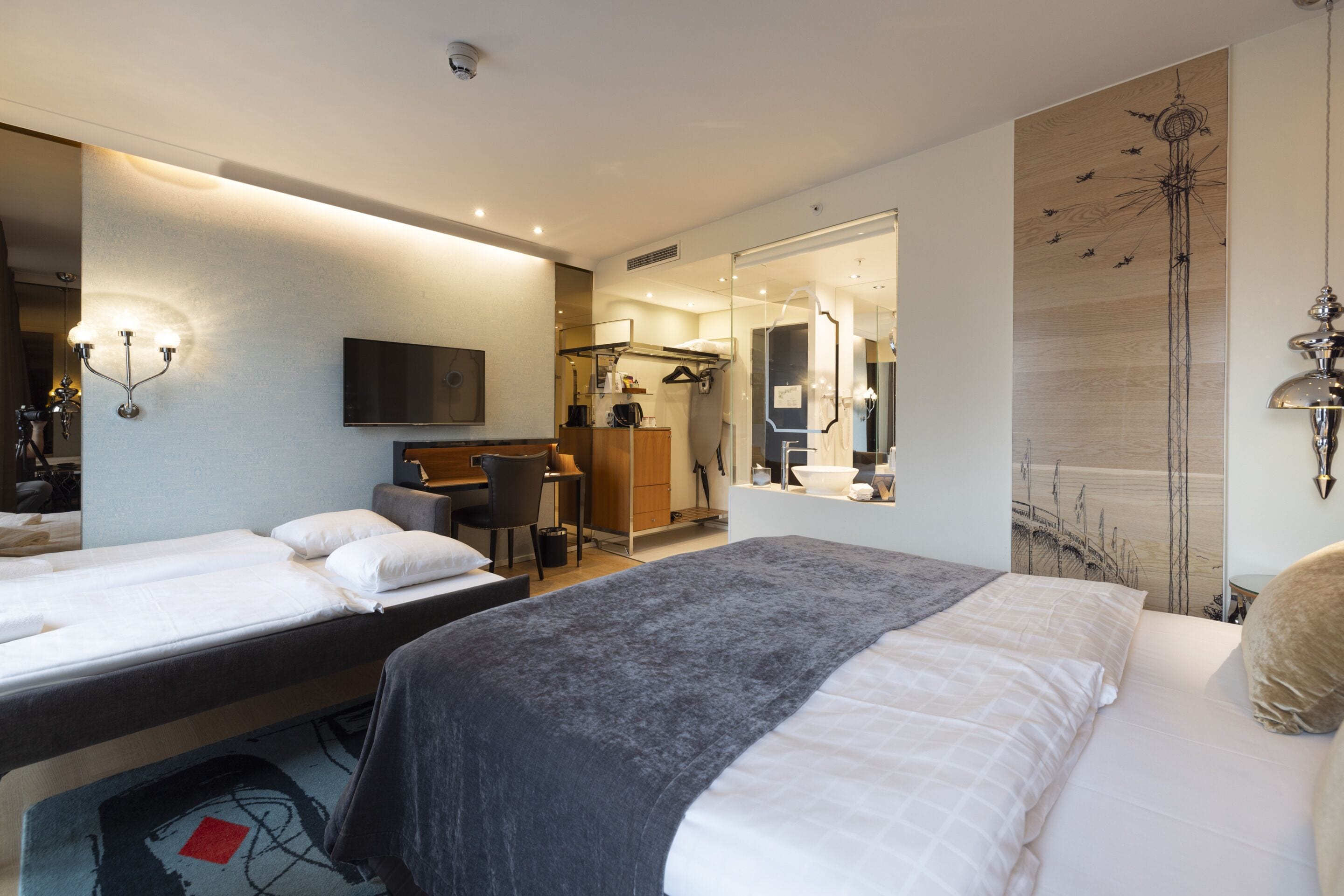 A hotel room with two beds, a desk, a chair, a mirror, and a television.