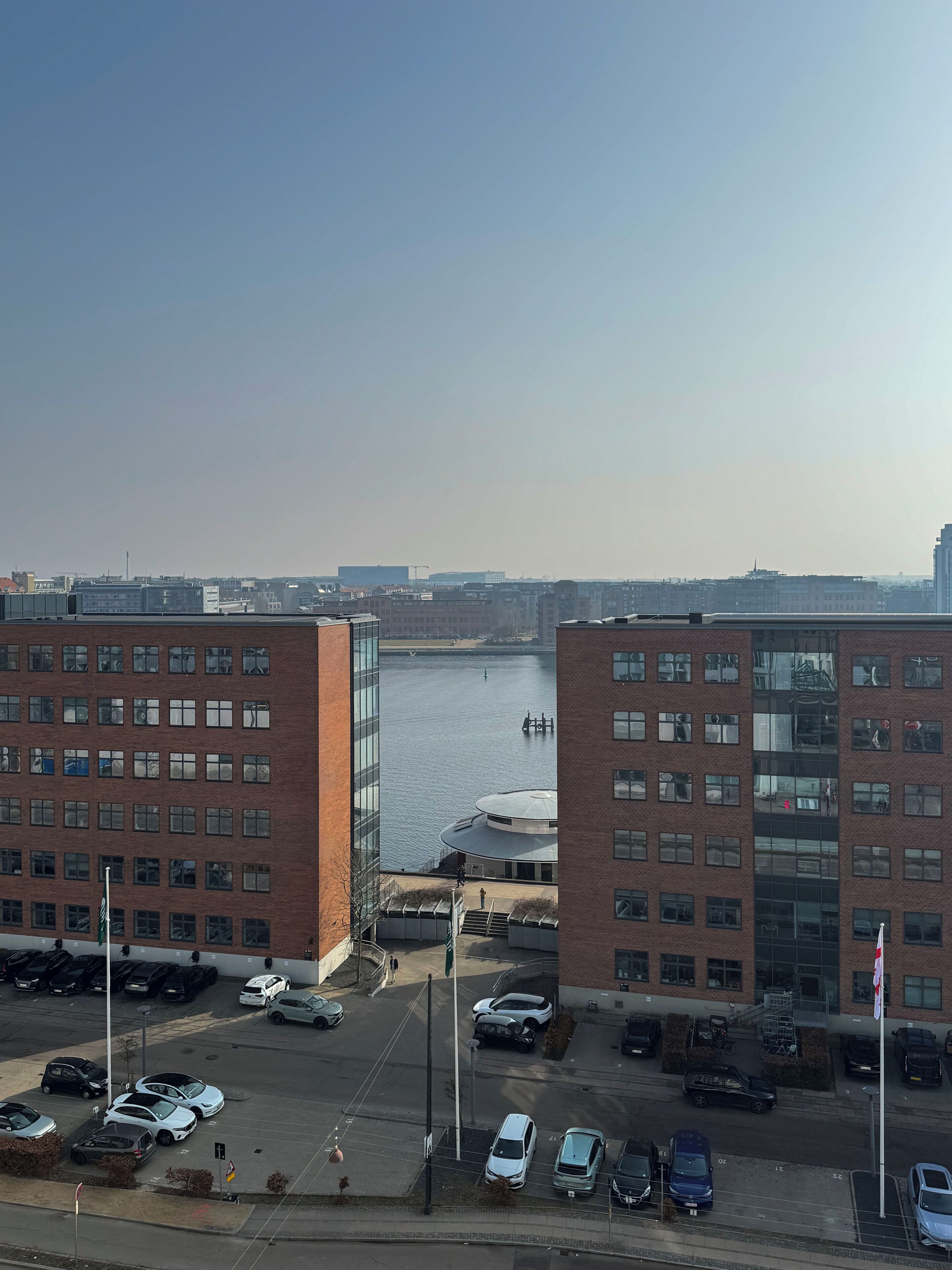 En høj bygning med udsigt over en flod og en parkeringsplads med flere biler.