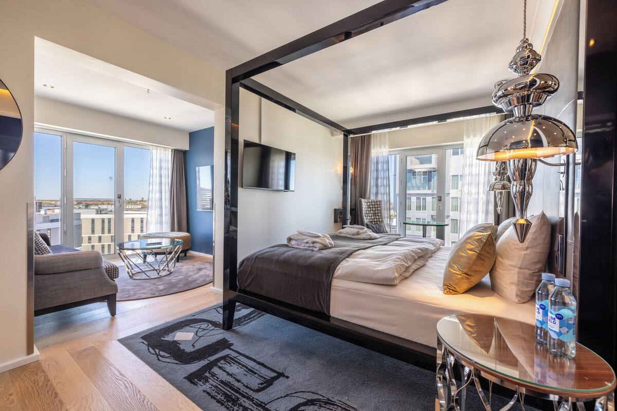 A modern hotel room with a large bed, a glass table, a sofa, and a TV.