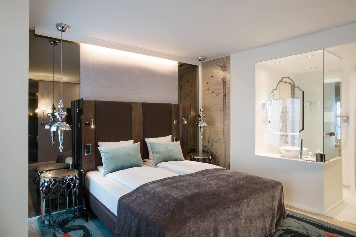 A modern hotel room with a large bed, a bedside table, a mirror, and a bathroom visible through an open door.