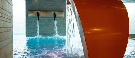 Ein moderner, überdachter Pool mit einer außergewöhnlichen, geschwungenen Wasserkreation und Blick zum Deckenraum.