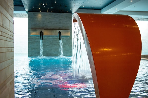 A modern indoor pool with a unique curved water feature and a view of the ceiling.