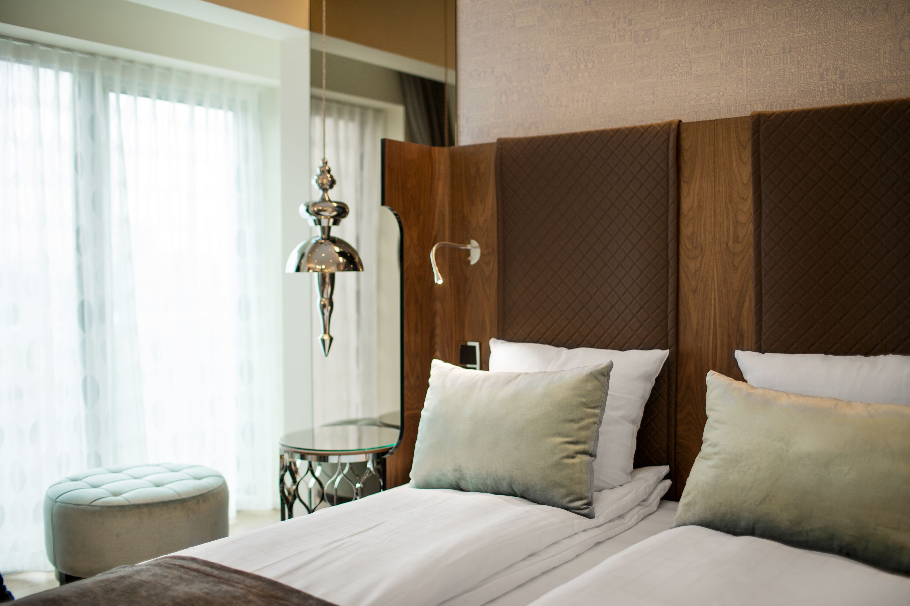 Hotelkamer met een groot bed, nachtkastje, hanglamp en uitzicht buiten door een raam met gordijnen.