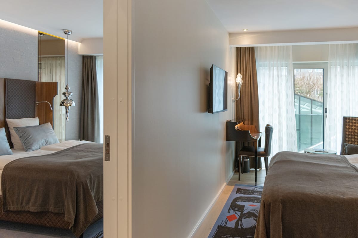 A hotel room with two beds, a desk, a chair, a TV, and a balcony with curtains.