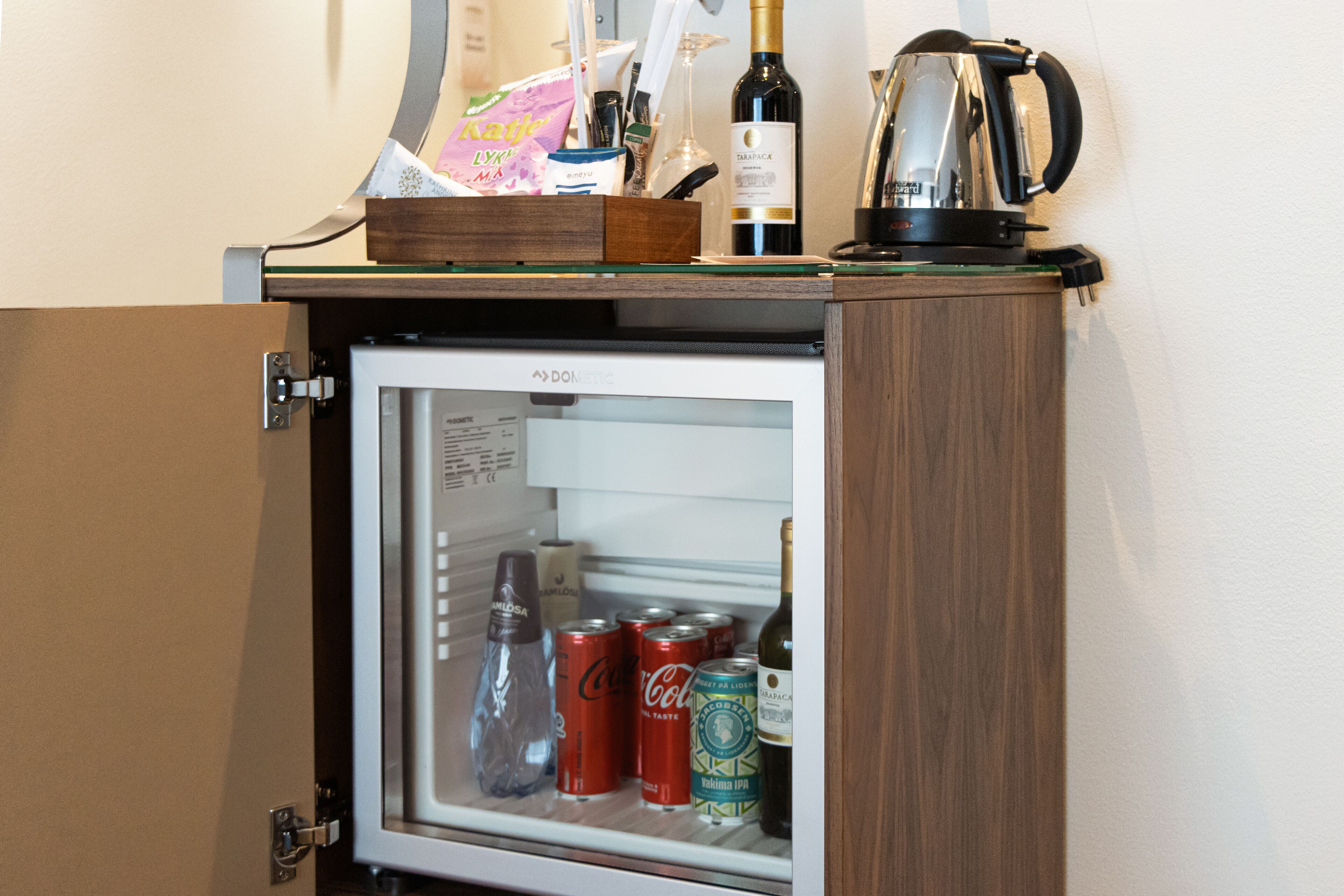 A minibar with a refrigerator containing beverages and a bottle of wine.