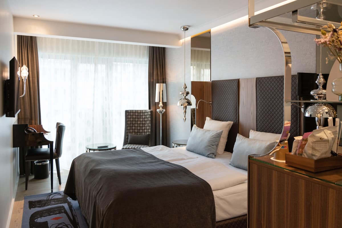 A modern hotel room with a large bed, a desk, and a chair.