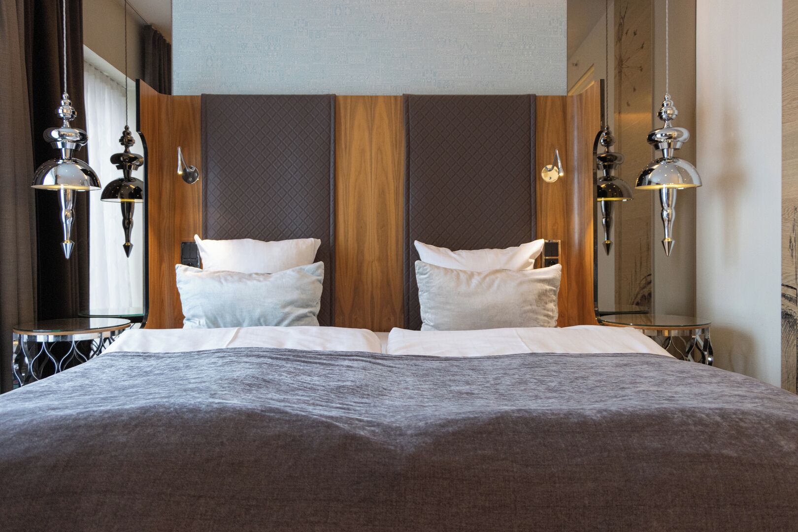 A modern hotel room with a large bed, two bedside tables, and a headboard with vertical wooden panels.