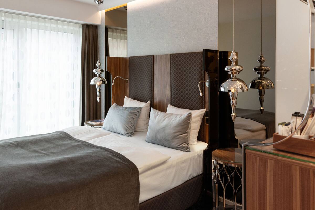 A modern hotel room with a large bed, a wooden headboard, a bedside table, and a mirror.