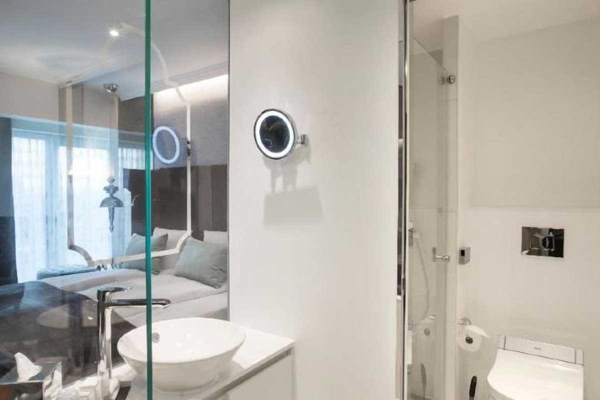 A modern bathroom with a glass shower enclosure, a round mirror, and a white sink.