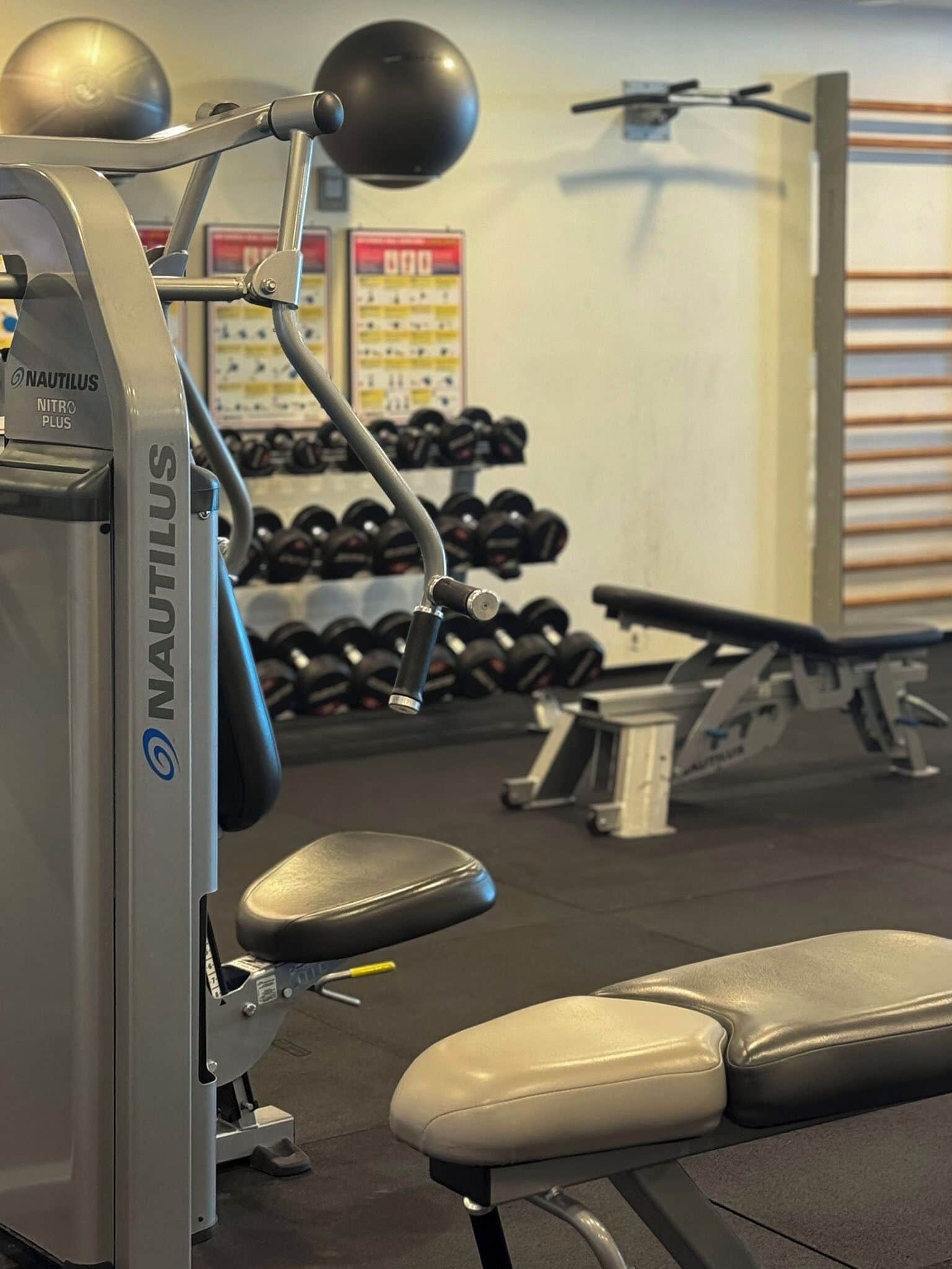 A Nautilus gym machine with a bench, dumbbells, and a wall-mounted mirror.