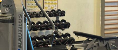 A Nautilus gym machine with a bench, dumbbells, and a wall-mounted mirror.