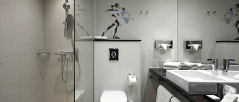 Un baño moderno con ducha de vidrio, inodoro blanco, lavabo con encimera de mármol y un espejo grande.