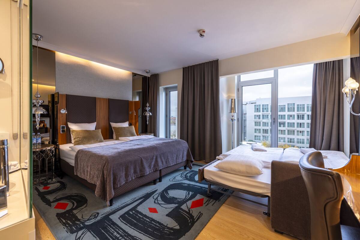 A hotel room with a large bed, a smaller bed, a desk, and a view of the city.