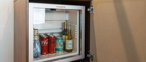 Un refrigerador pequeño con puerta de vidrio, que contiene una botella de vino, una lata de Coca-Cola y una botella de agua.