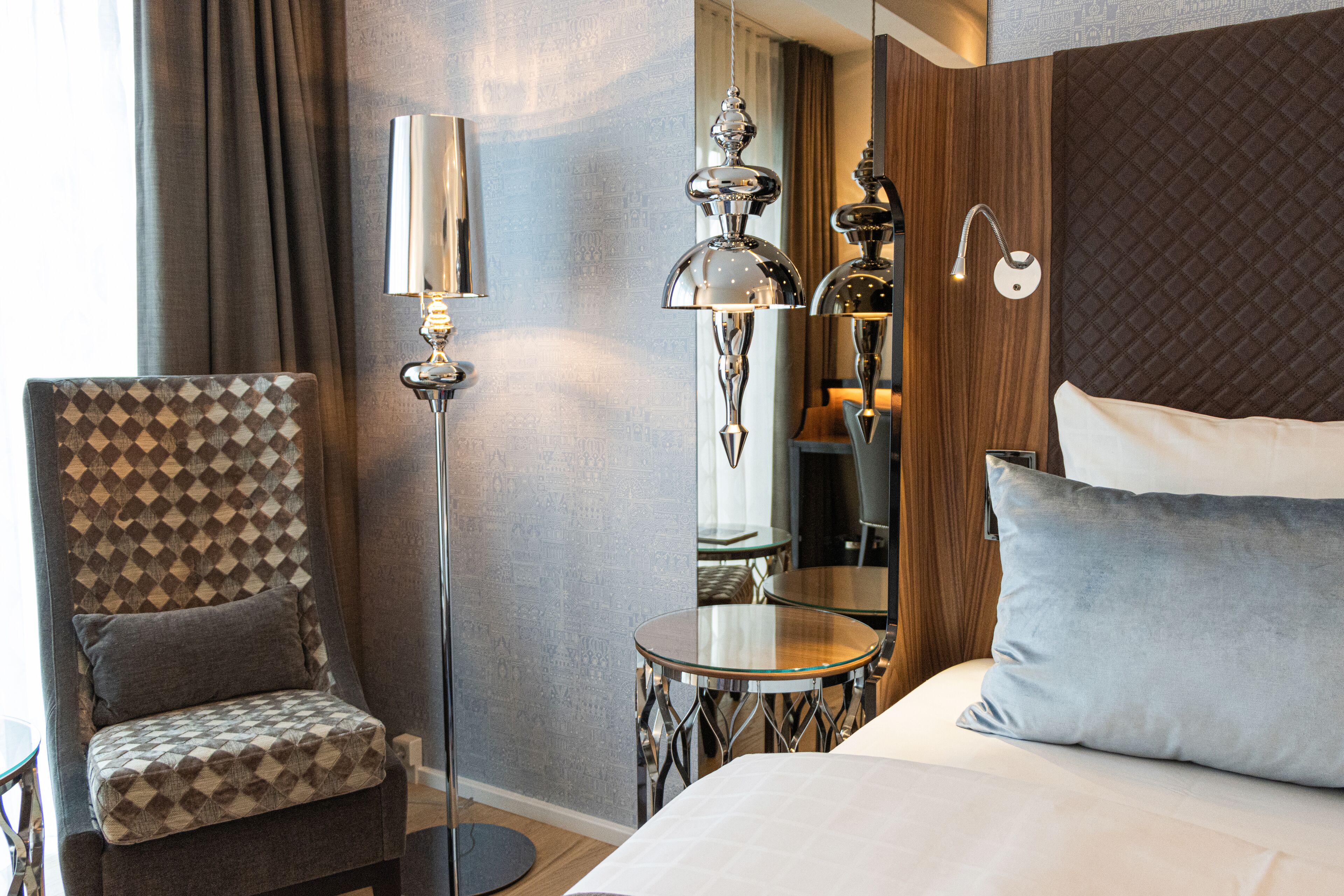 A hotel room with a bed, a chair, a lamp, and a small table.