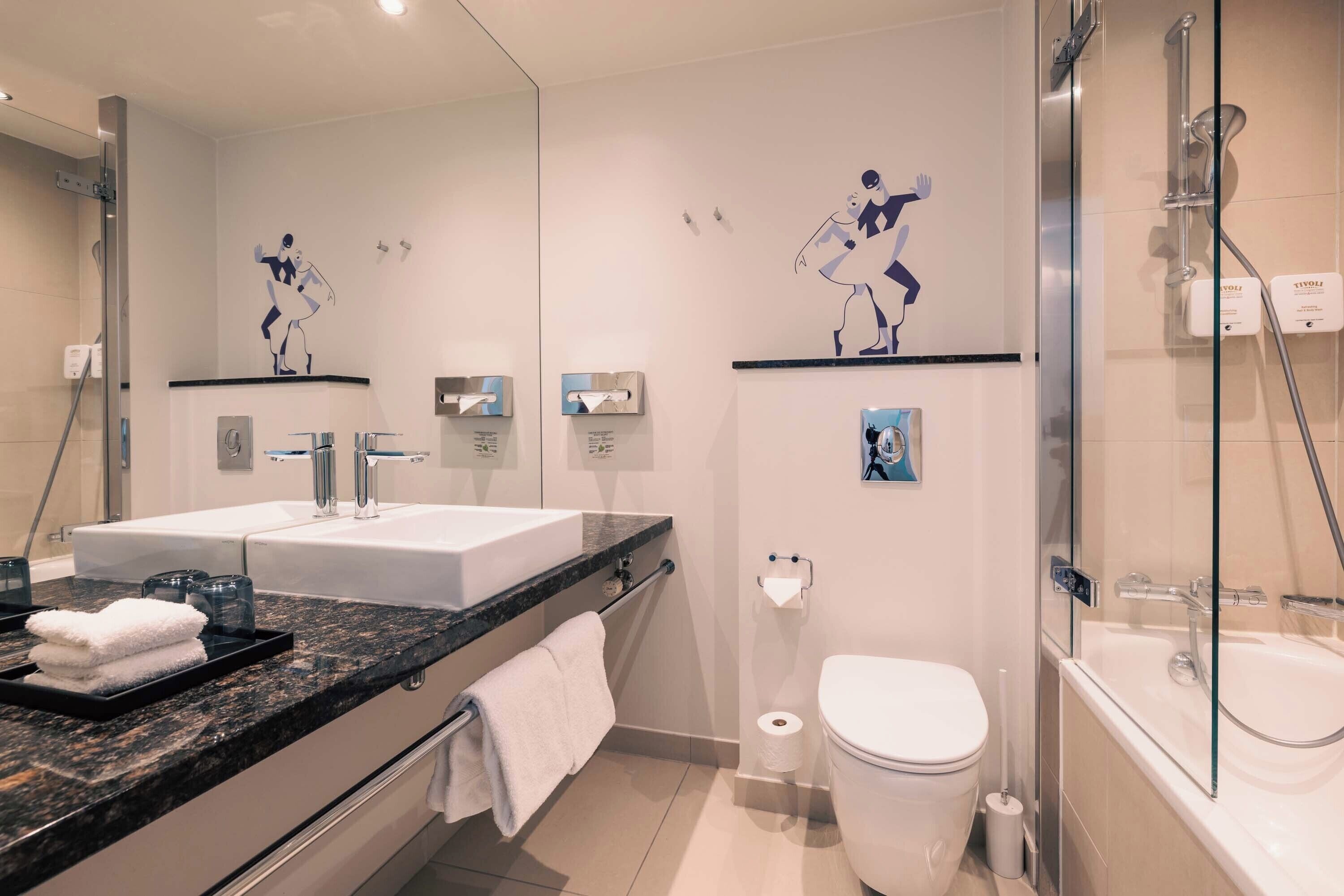 Un baño moderno con lavamanos dobles, cabina de ducha de vidrio y detalles decorativos en las paredes.