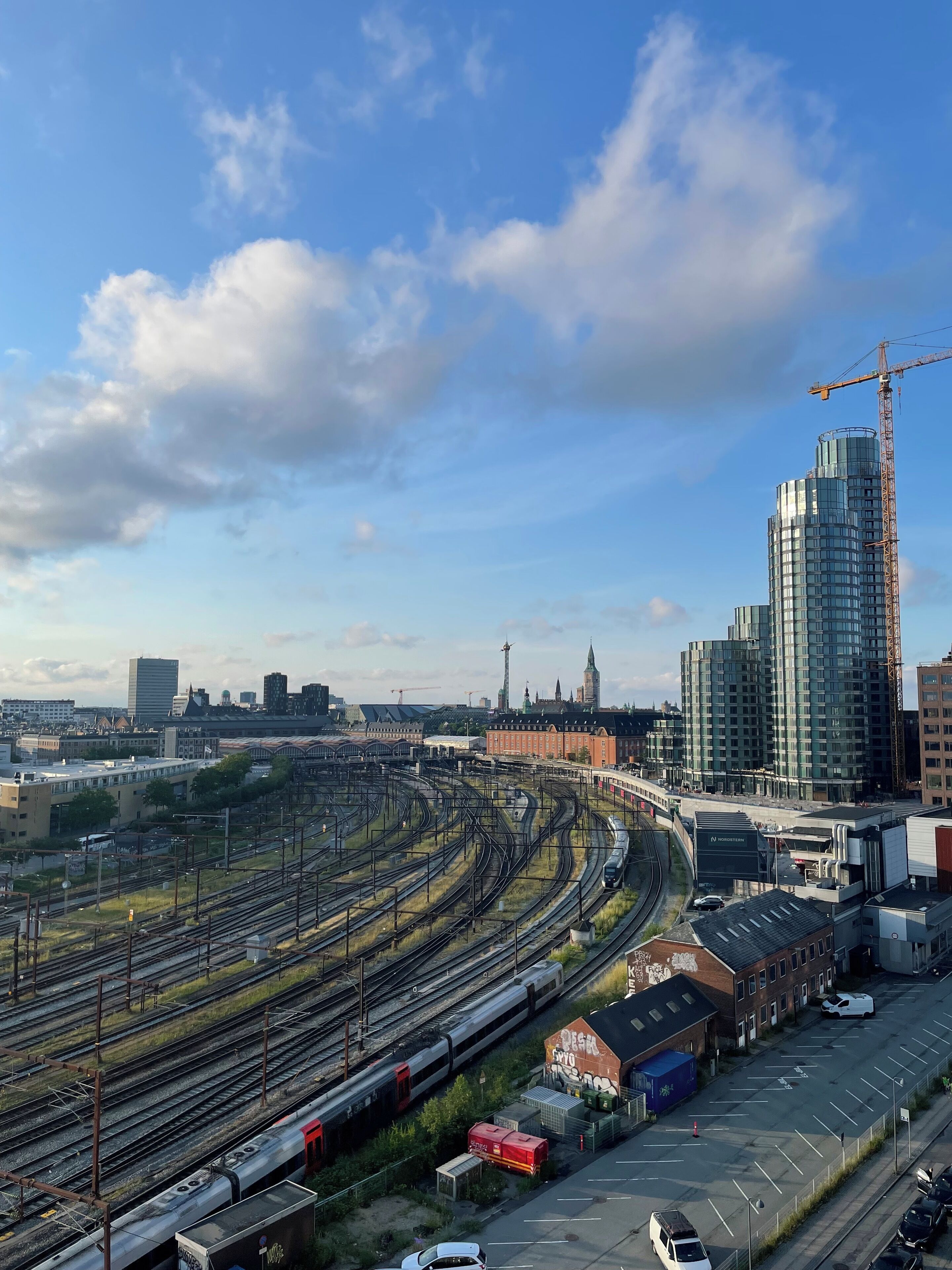 A railway station with multiple tracks, a train, and surrounding buildings including a tall construction crane.