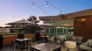 Un espacio al aire libre con patio, mesas, sillas, sombrillas y luces colgantes.