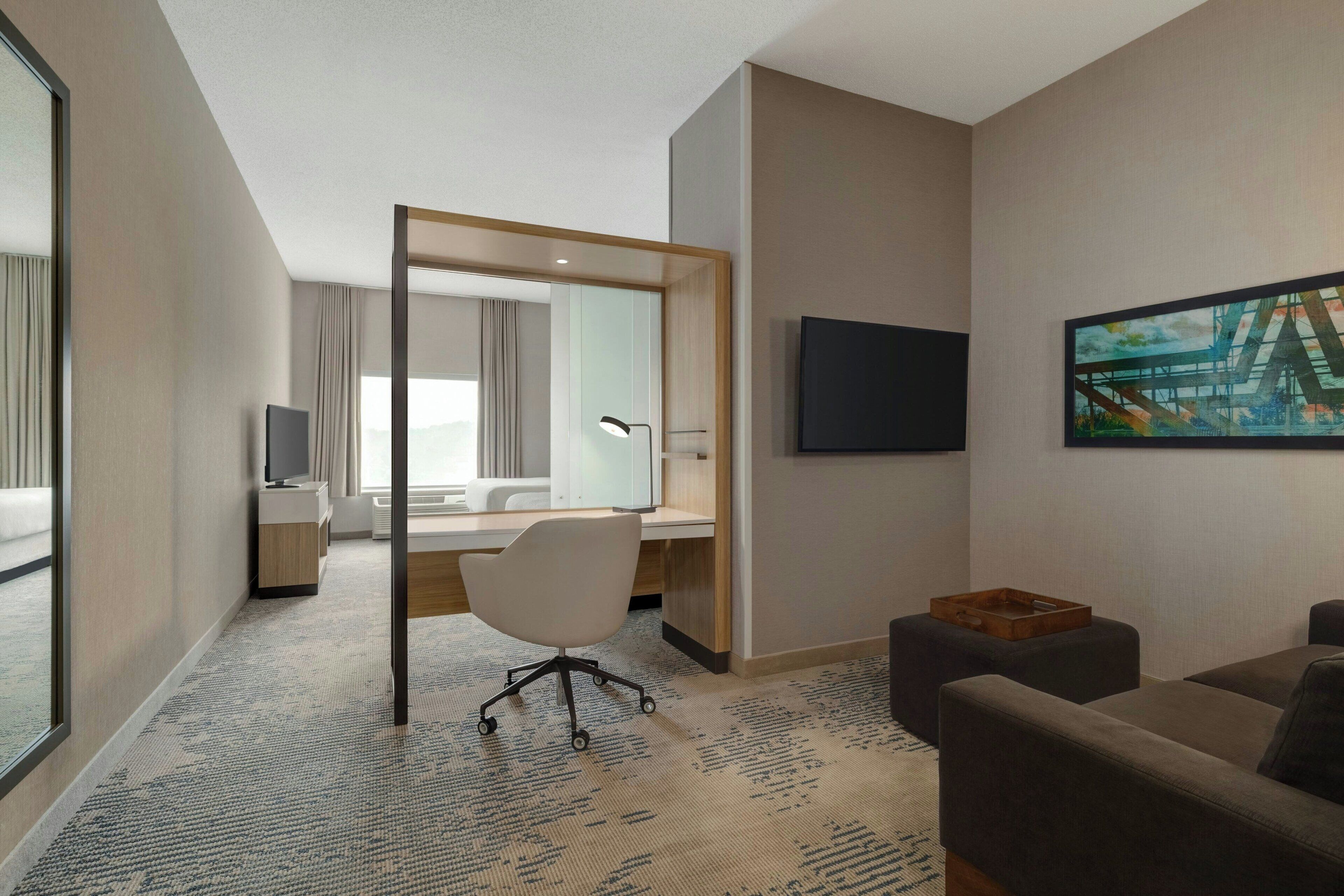 A hotel room with a large bed, a desk with a chair, a TV, and a painting on the wall.