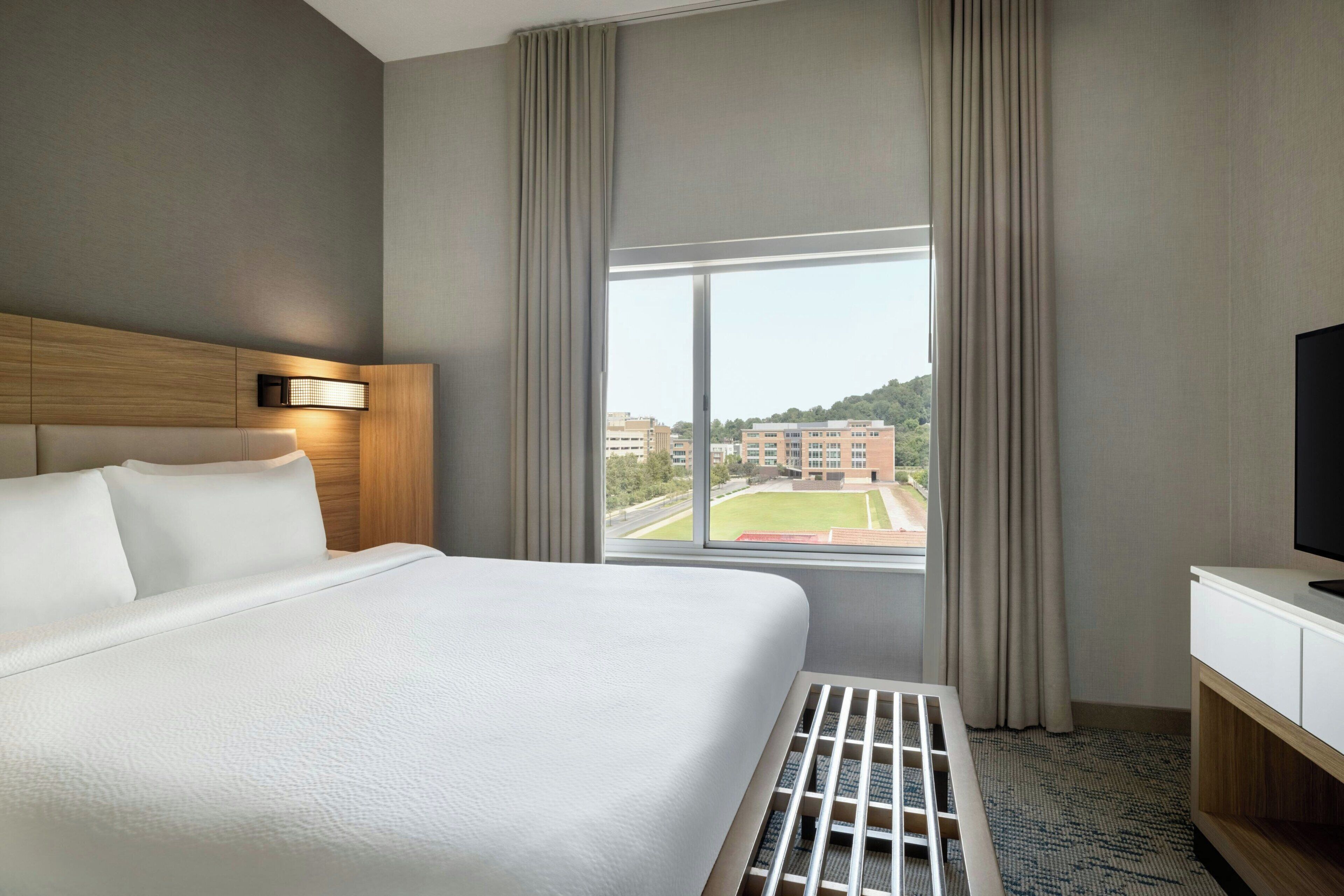 A hotel room with a large bed, a TV, and a window with curtains.