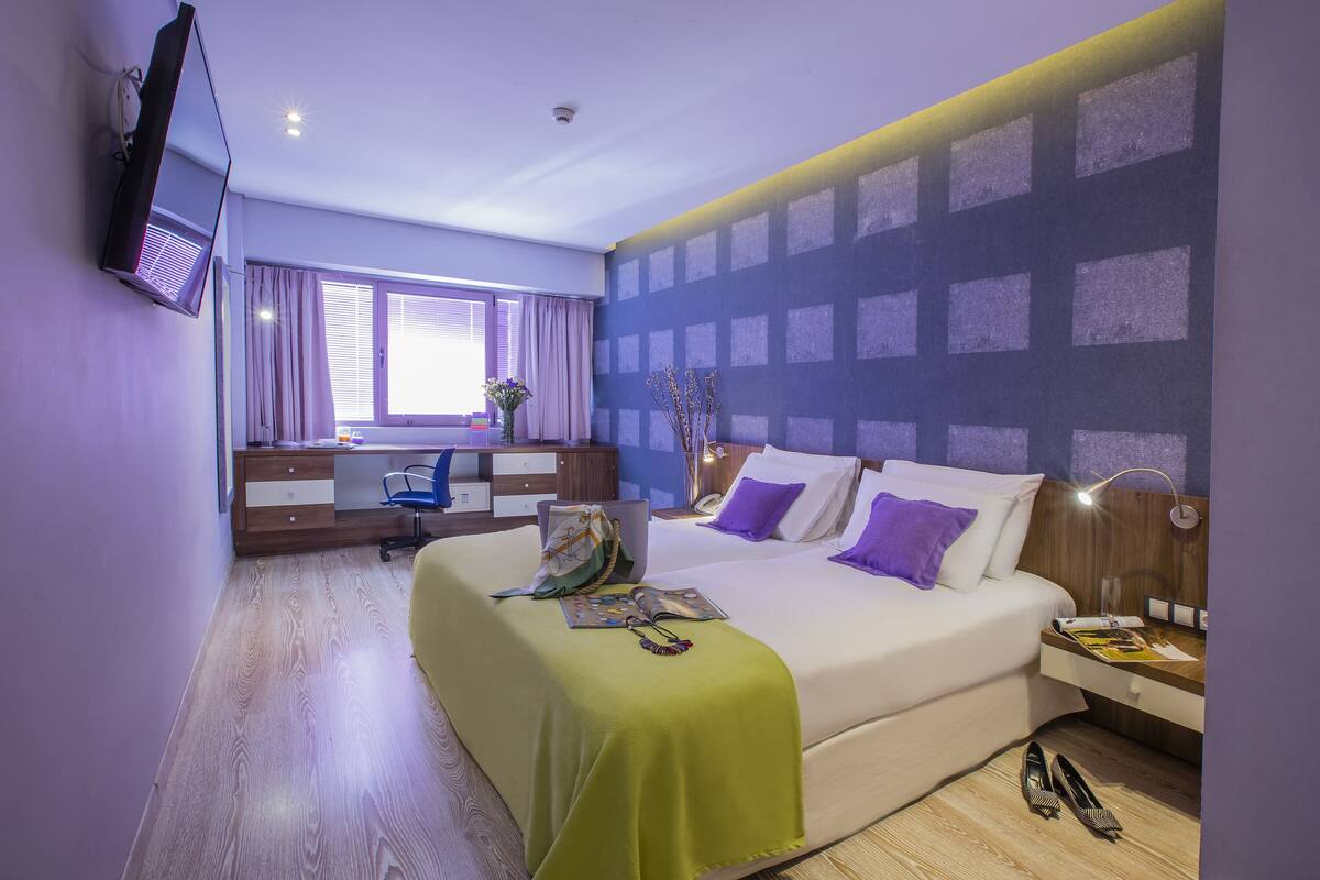 Una habitación de hotel con cama, escritorio y televisión en la pared.