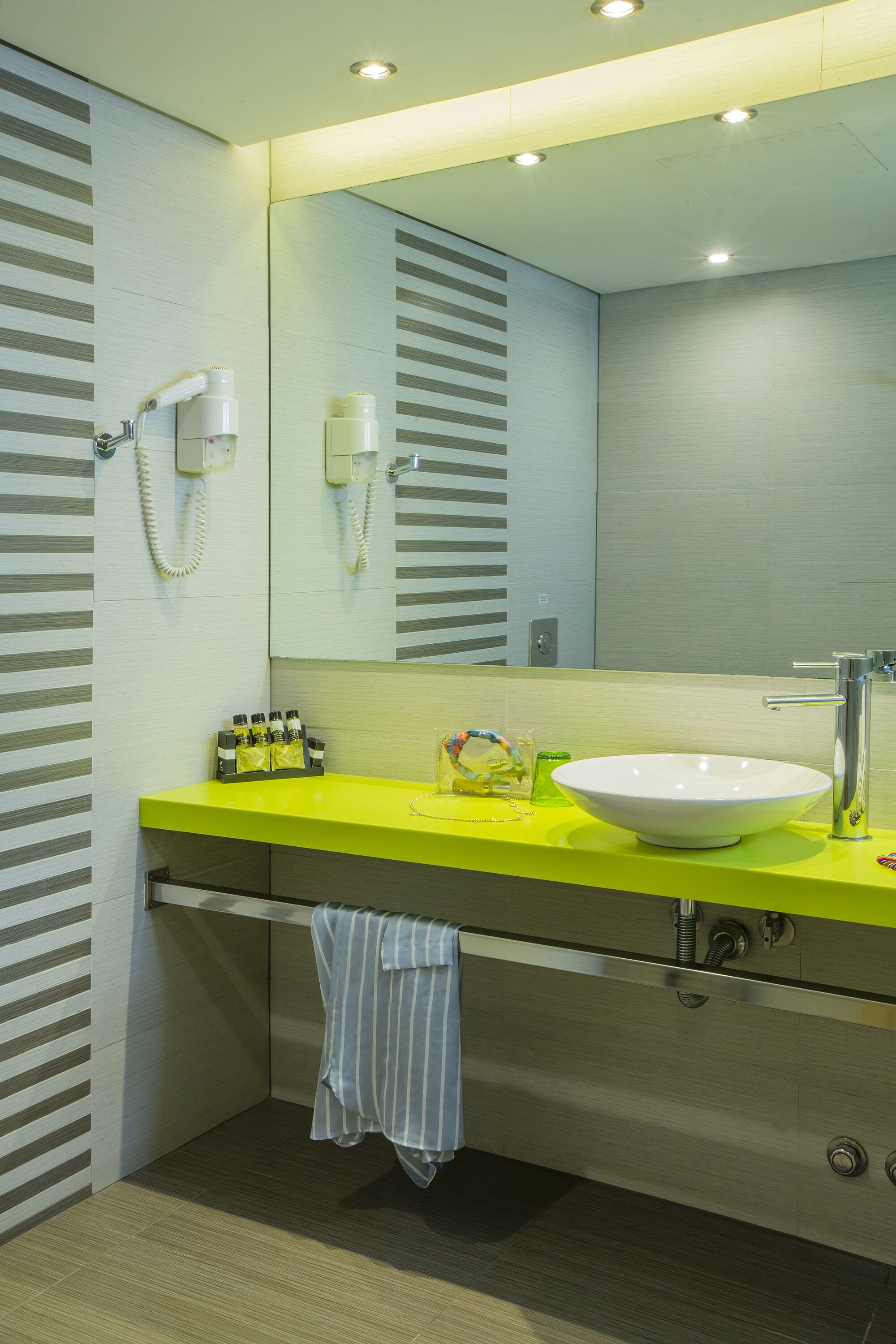 A modern bathroom with a large mirror, a white sink, and a bright yellow countertop.