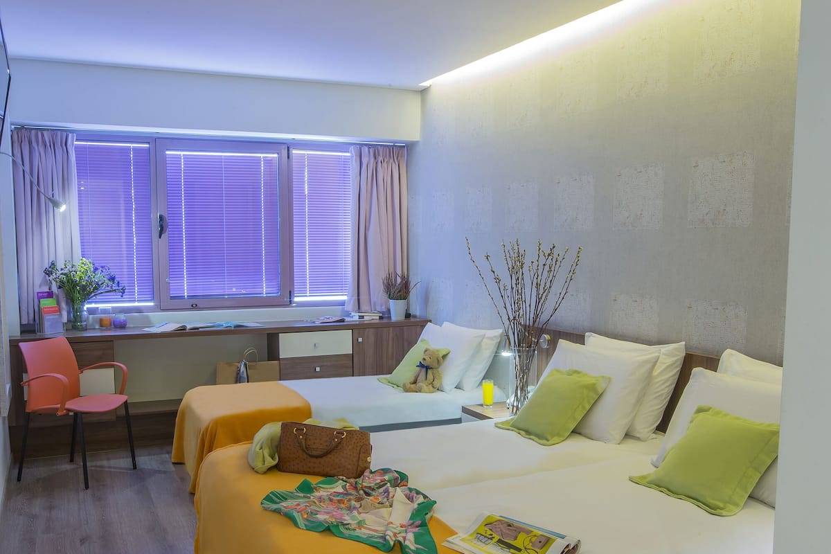 Habitación de hotel con cama, dos mesitas de noche, un escritorio, una silla y una ventana con cortinas.