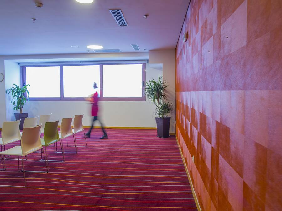 A conference room with a red carpet, multiple chairs, and potted plants.