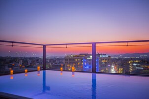 Piscina infinita no terraço com vista para a cidade ao pôr do sol.