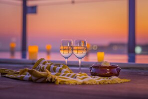 Two glasses of white wine on a wooden table with a striped cloth, a small pot, and candles in the background. - Novus City Hotel (Athens)