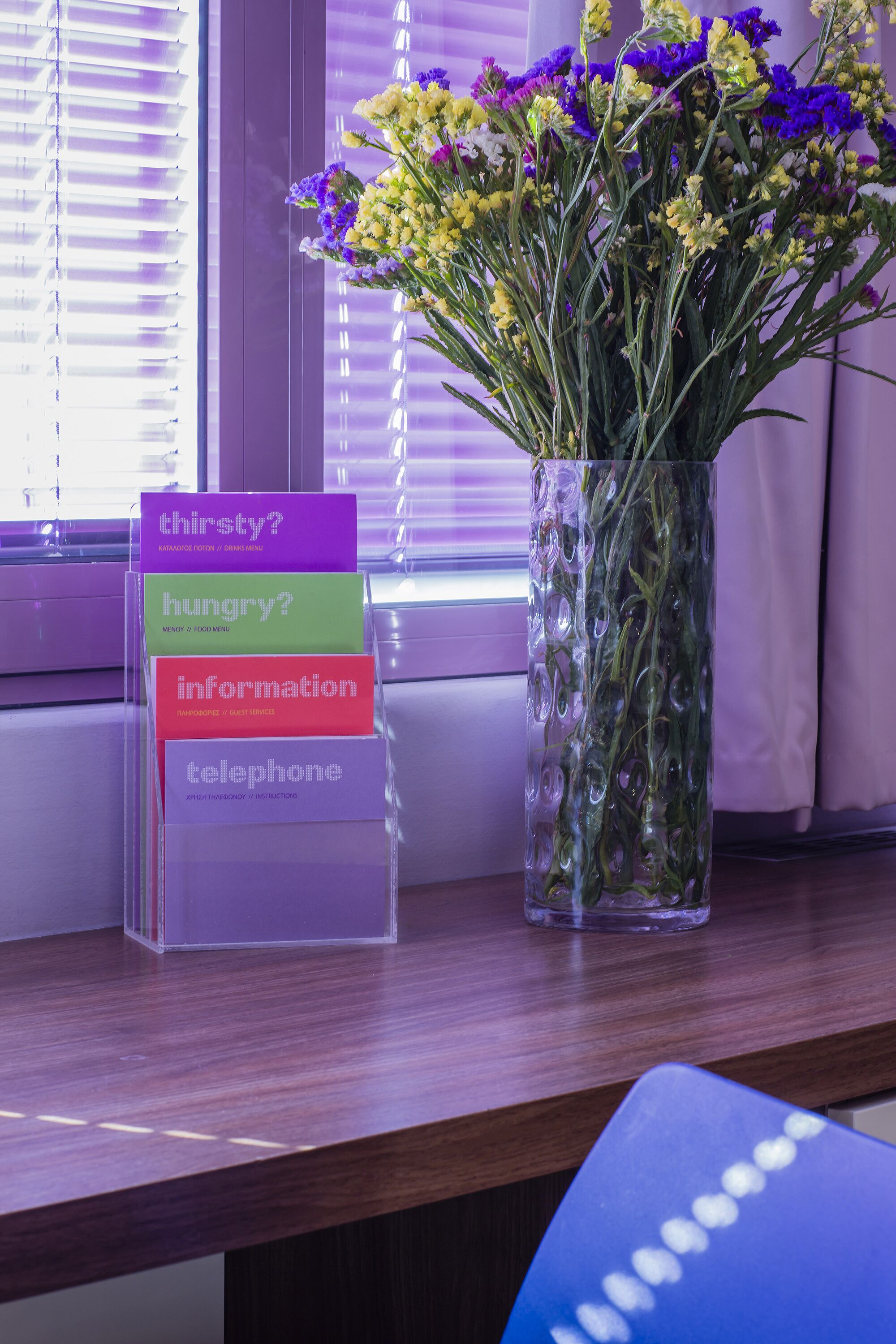 Un escritorio con un jarrón de flores y un cartel con opciones como '¿sed?','¿hambre?','información' y 'teléfono'.