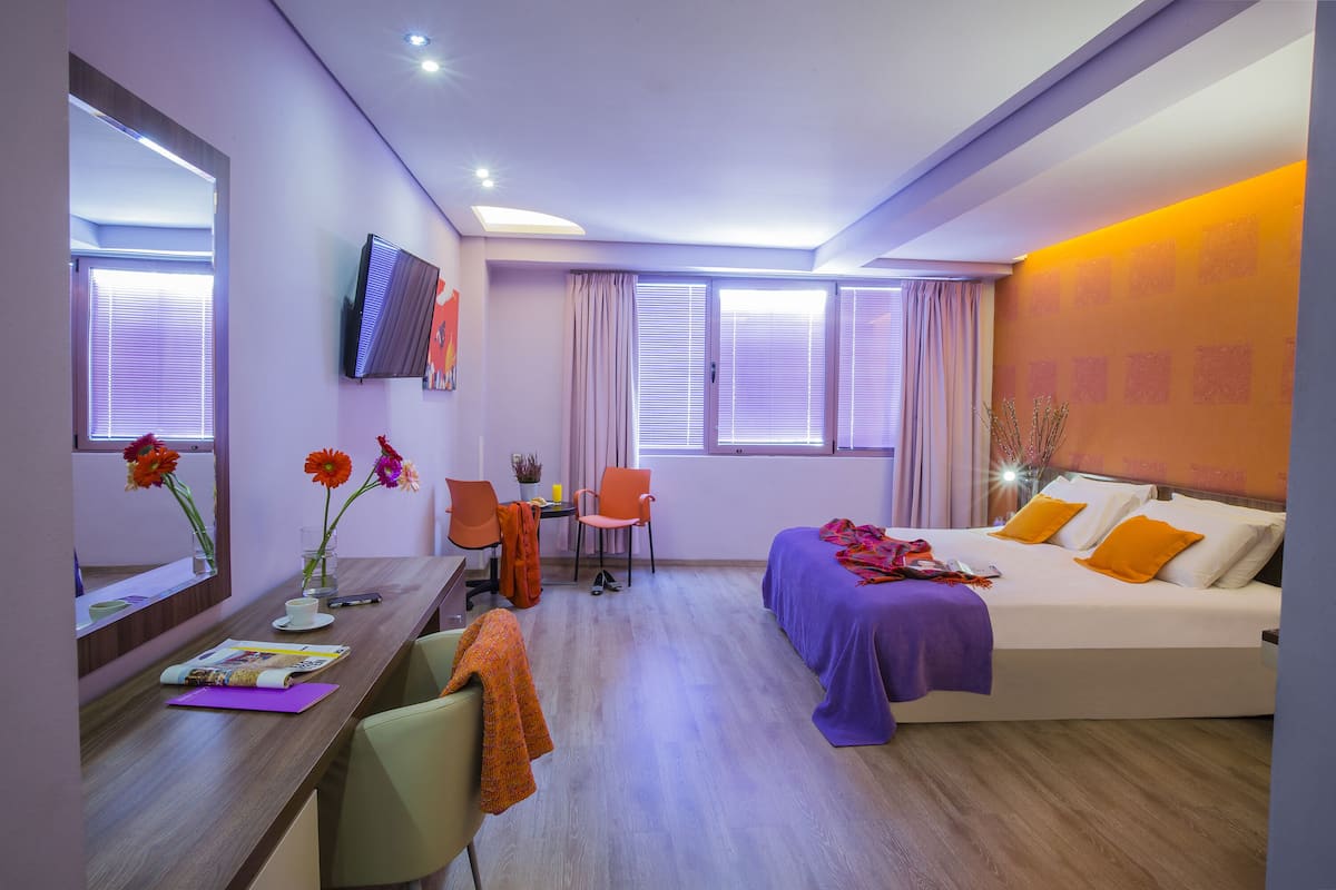 Habitación de hotel con cama, escritorio, silla y televisor en la pared.