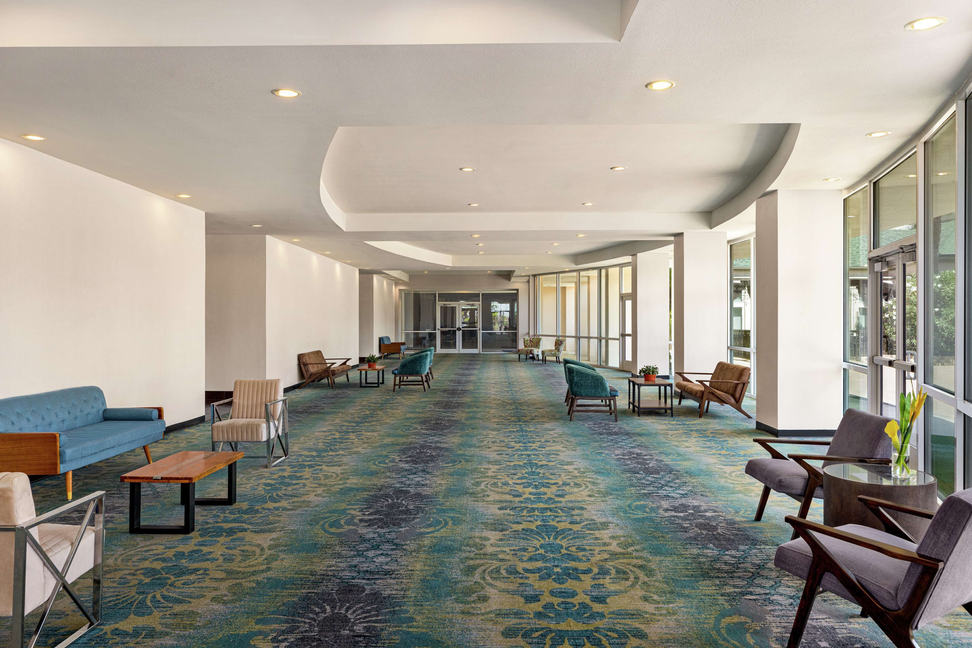A spacious lobby with a patterned carpet, seating areas, and large windows.