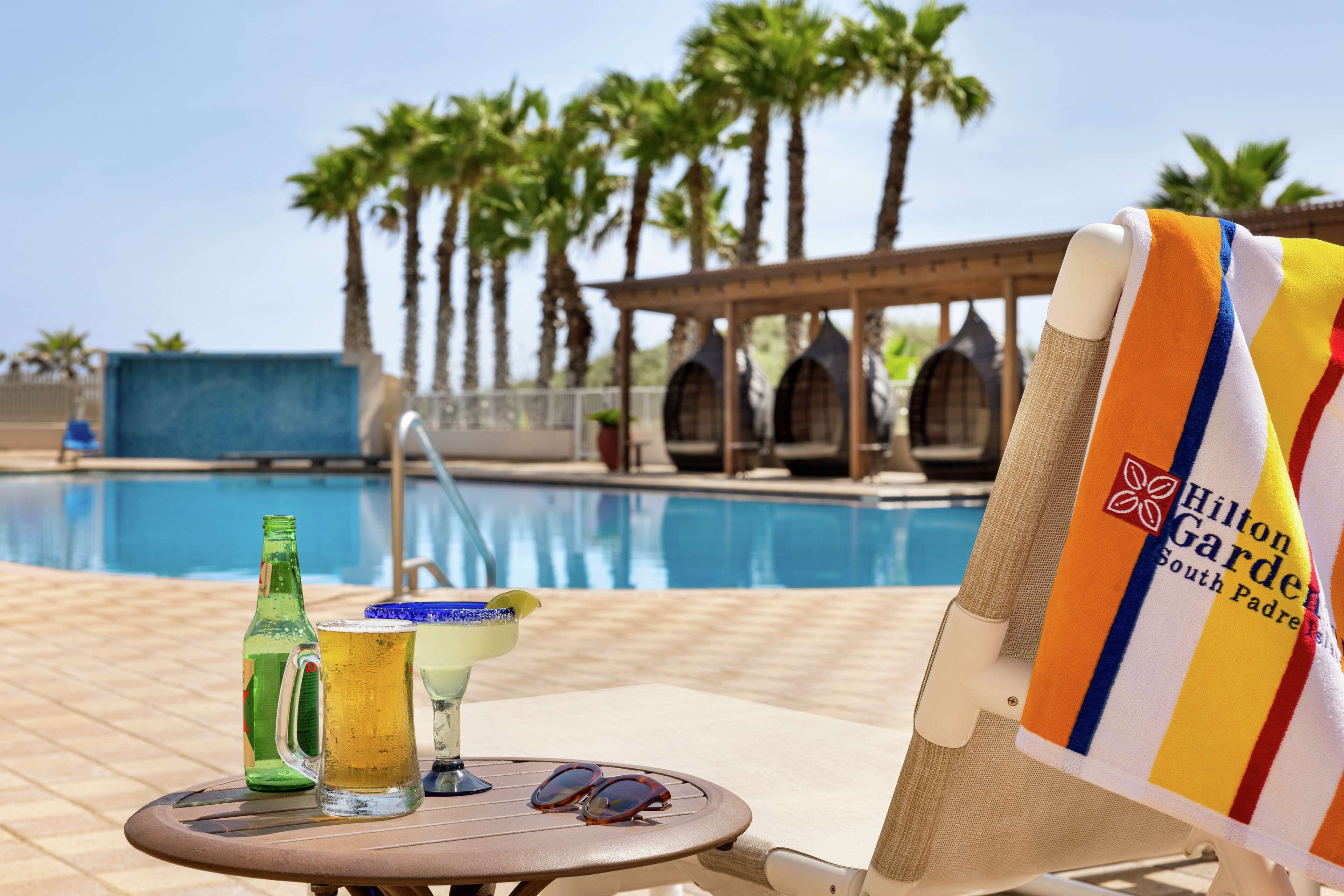 A poolside setting with a lounge chair, a table with drinks, and a pool in the background.