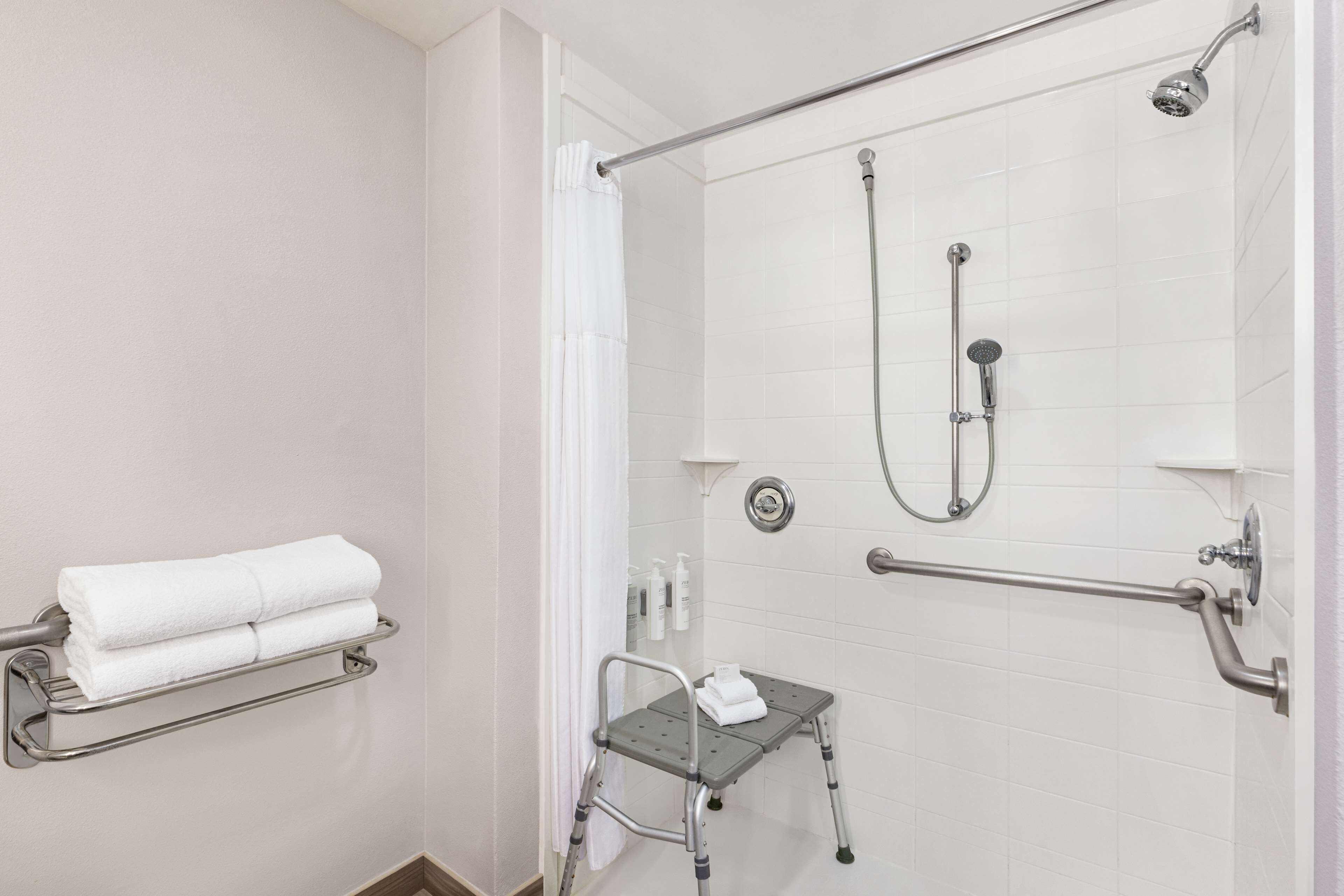 Een moderne badkamer met een douche zonder drempel, handgrepen, een klein opstapkrukje en een handdoekhouder.