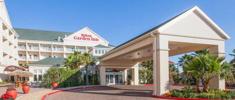 A hotel entrance with a covered walkway, palm trees, and a sign for Garden Inn.