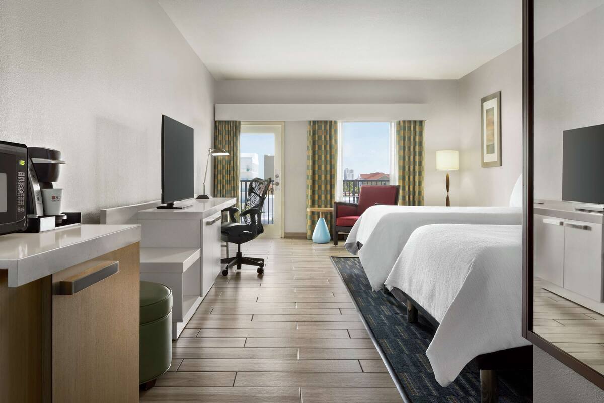 A hotel room with a bed, desk, chair, and a coffee machine.