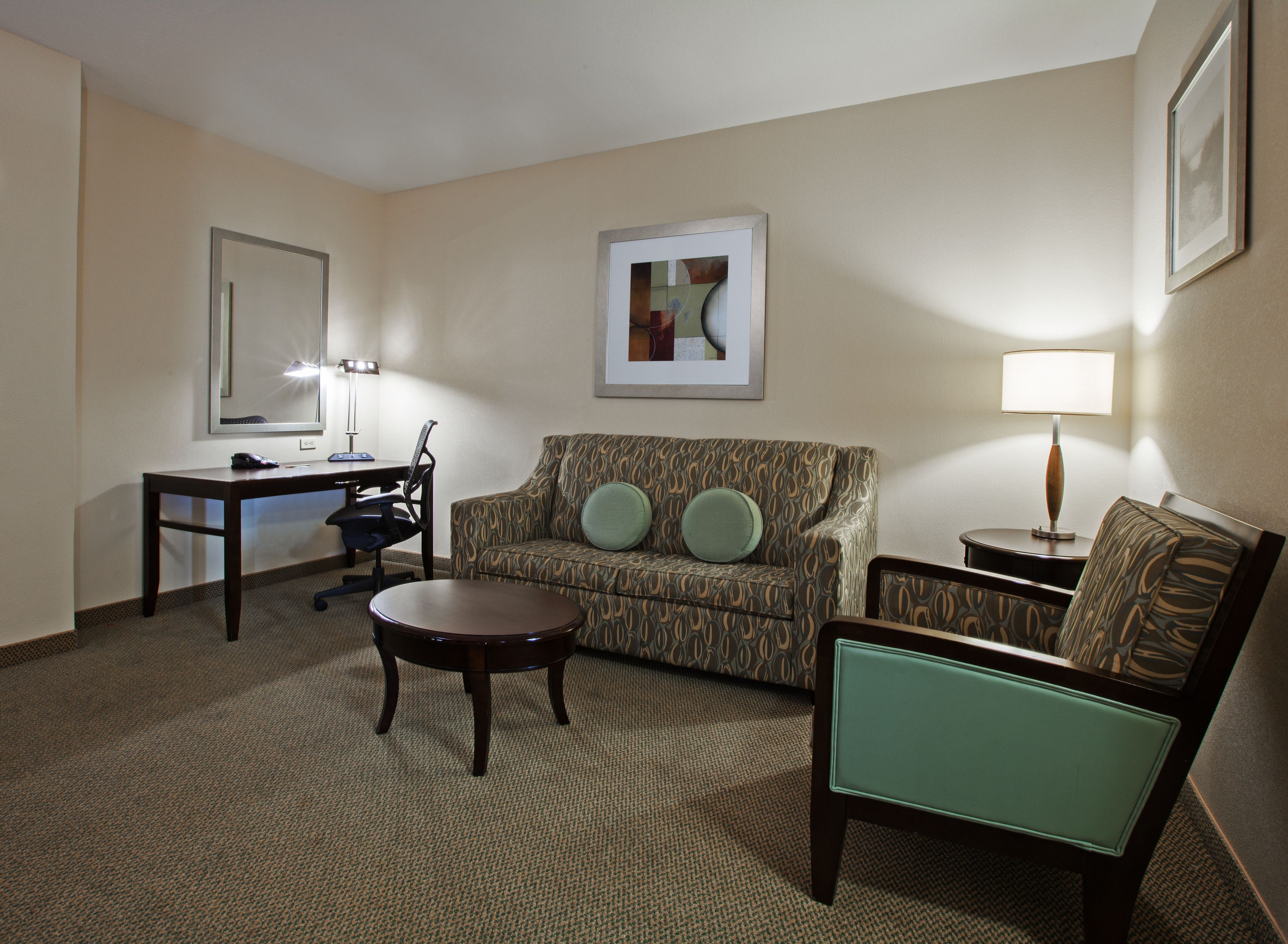 A hotel room with a sofa, armchair, desk, and lamp.