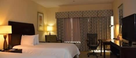 A hotel room with two beds, a desk, a chair, a television, and a window with curtains.