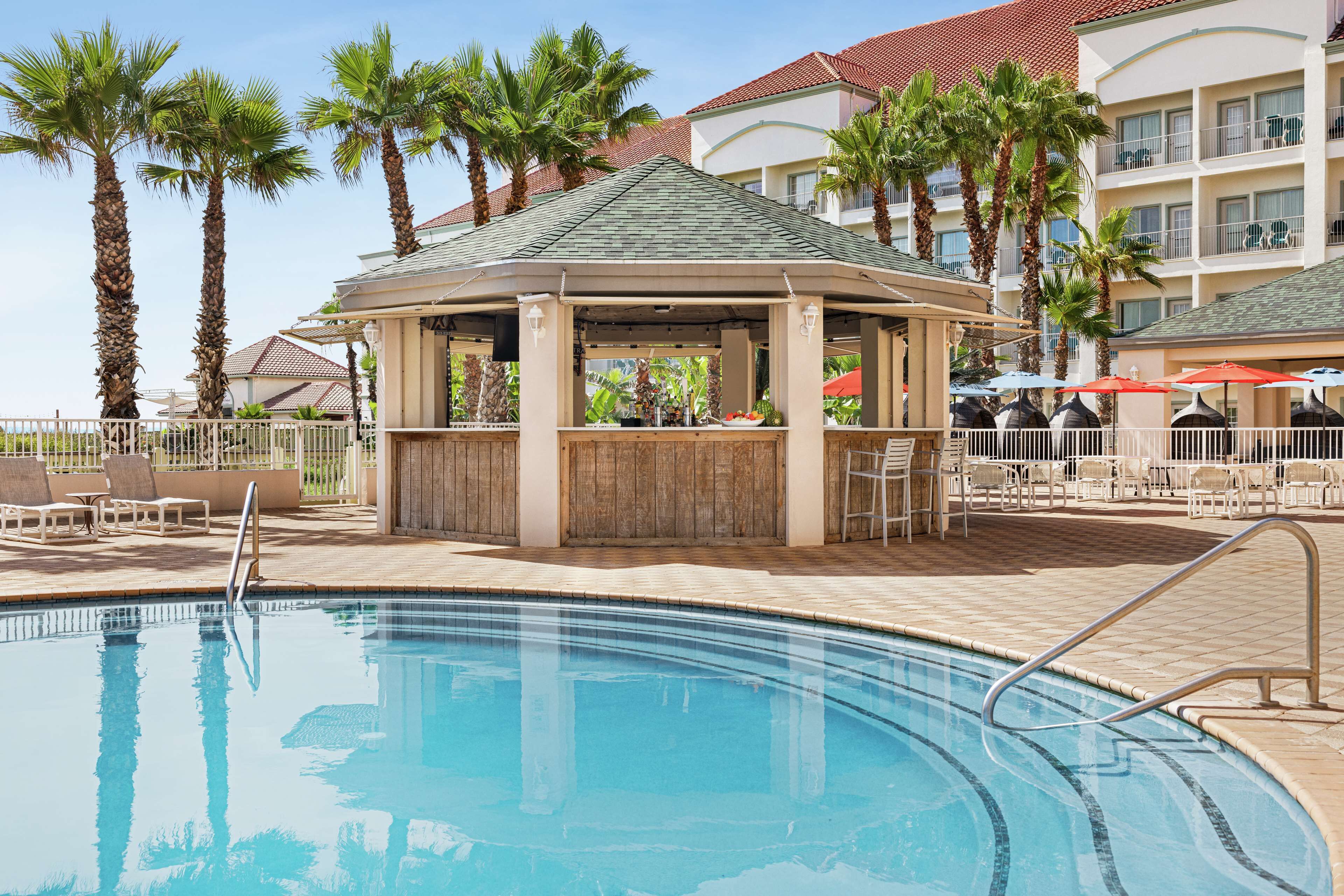 A pool area with a gazebo, palm trees, and a building with balconies.