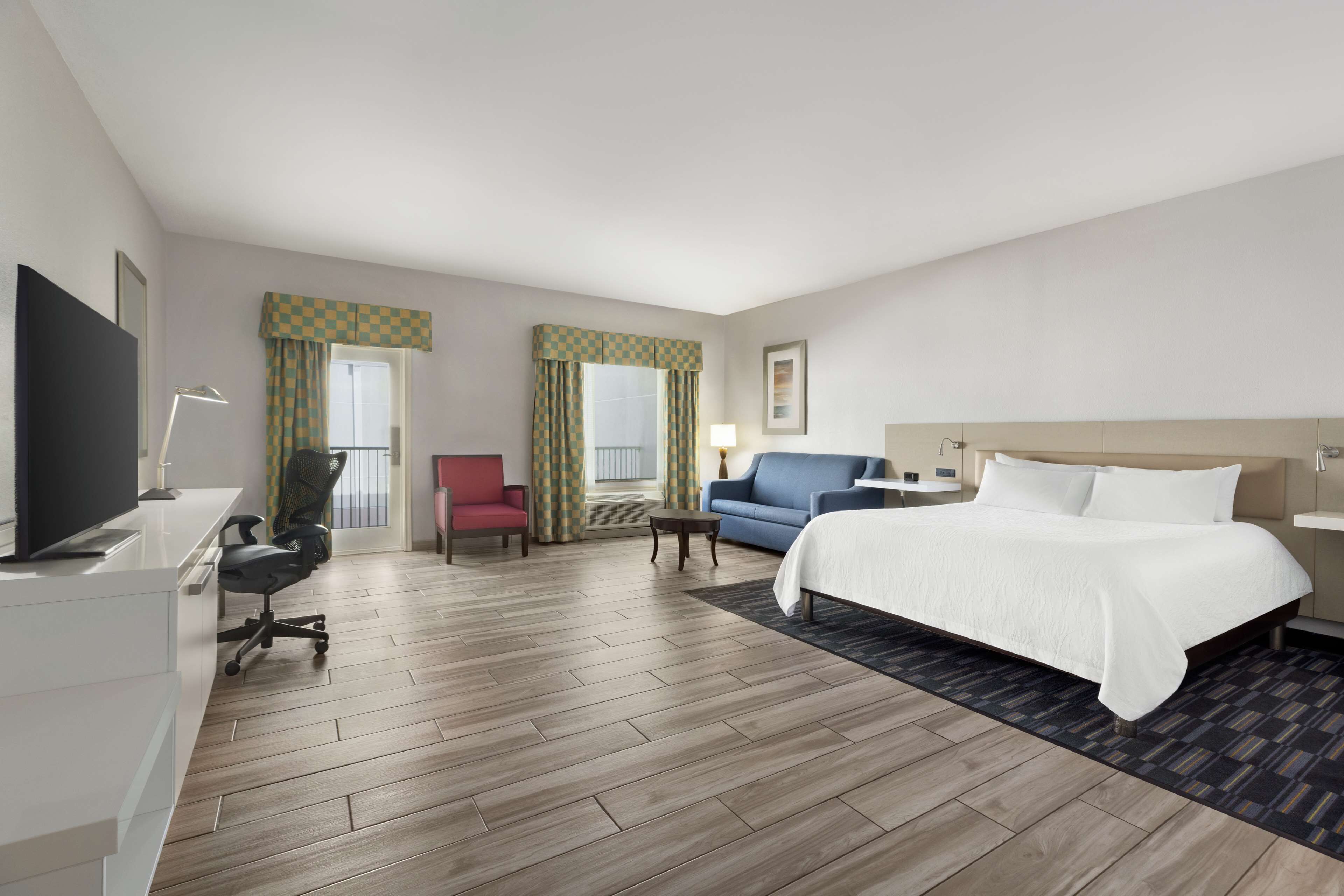 Ein Hotelzimmer mit Bett, Schreibtisch mit Stuhl, Fernseher, Sofa und kleinem Tisch.