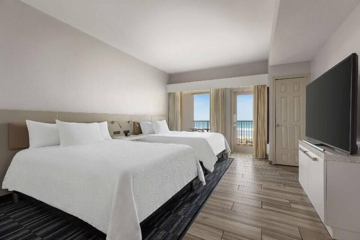 A hotel room with two beds, a TV, a balcony with a view, and a door leading outside.
