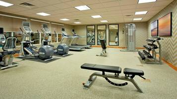 Une salle de sport équipée de tapis de course, de vélos elliptiques, d’un banc de musculation et d’appareils de musculation.