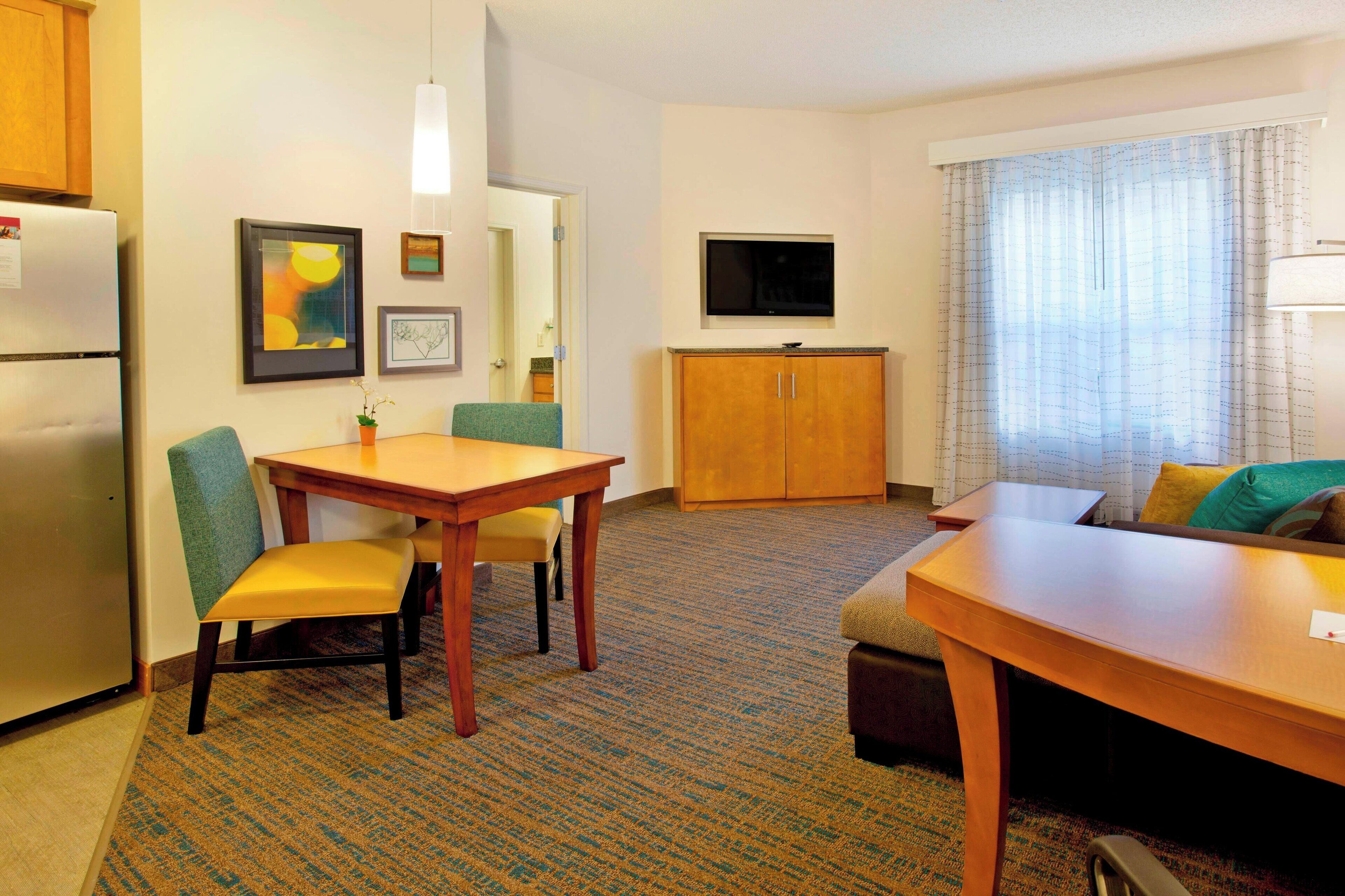 A hotel room with a dining table, two chairs, a sofa, a TV, and a cabinet.