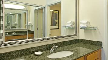 A bathroom with a granite countertop, a white sink, a large mirror with a decorative frame, and a towel rack with folded towels.