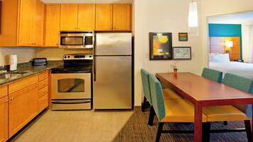A compact kitchen with wooden cabinets, stainless steel appliances, and a dining area with a table and chairs.