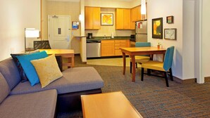 A compact hotel room with a sofa, a small dining table, a kitchenette, and a door leading to a bathroom. - Residence Inn Bridgewater Branchburg (Branchburg)