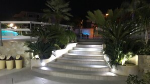 Un escalier extérieur éclairé, conçu pour la nuit, avec des marches illuminées, entouré de plantes en pot et d’un espace piscine.